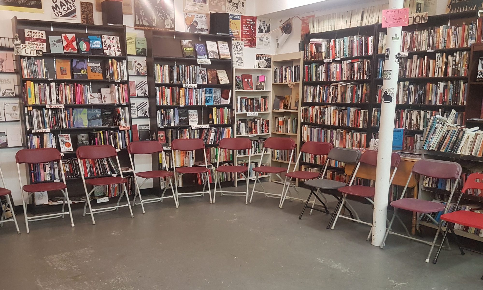 Image of store setup for an event. A circle of about a dozen folding chairs. Behind them are bookcases and the walls are decorated with posters.